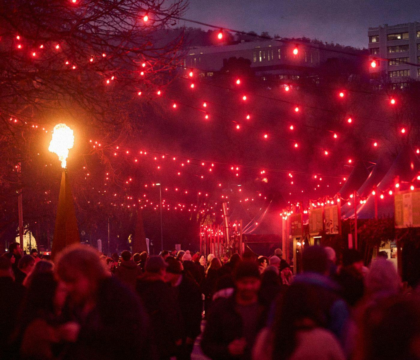 A large crowd of people outside under red string lights at Winter Feast.